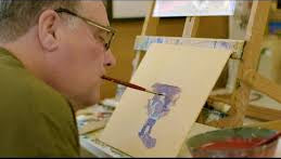Person painting a figure on paper with an easel and art supplies around