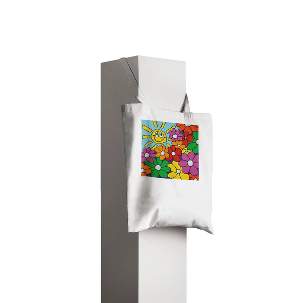 A durable white canvas tote bag featuring an original mouth-painted illustration by MFPA artist Lars Hollerer. The design shows a vibrant garden of colorful flowers and a cheerful, smiling sun against a bright blue sky.